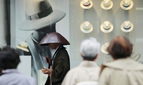 Seorang biksu berdoa di depan jendela  pusat perbelanjaan di Ginza, Tokyo, Jepang. Wisata belanja kini menjadi bagian dari liburan banyak orang.