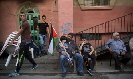 Seorang bocah laki-laki Palestina memegang bendera Palestina sambil duduk di pangkuan ayahnya di luar rumah keluarga ohammed Ali (19 tahun) di kamp pengungsi Shuafat di Yerusalem. Indonesia berkomitmen untuk meningkatkan bantuan kemanusiaan bagi Palestina. Ilustrasi. 