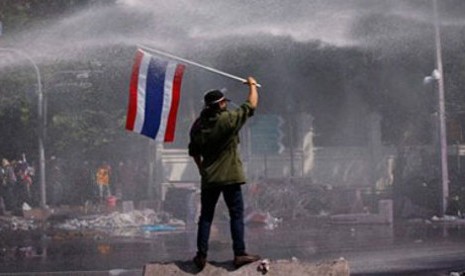 Seorang demonstran anti-pemerintahan Thailand mengibarkan bendera di tengah semprotan water canon pasukan antihuru-hara pemerintah.