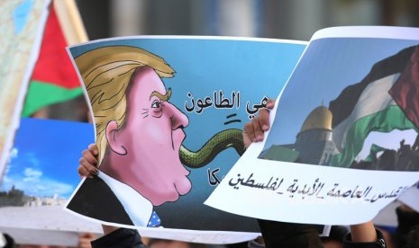 Seorang demonstran memegang poster kartun  Presiden AS dan sebuah foto kubah batu di dalam Masjid Al-Aqsa  yang bertuliskan Yerusalem adalah ibukota abadi Palestina dan Amerika adalah sebuah bencana ,di luar Kedutaan Besar AS di Amman, Yordania,