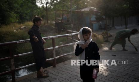 Seorang anak perempuan menunggu teman-temannya saat mereka berjalan ke sekolah di Kabul, Afghanistan, Ahad (12/9).