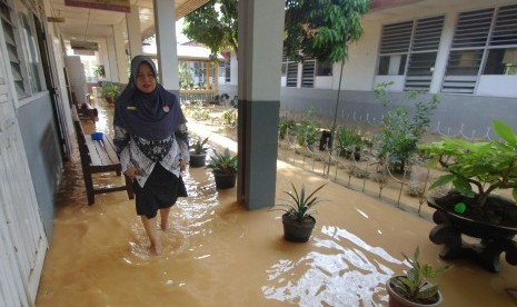 Seorang guru berjalan melewati genangan banjir yang masih merendam sekolah di Batipuhpanjang, Padang, Sumatera Barat, Rabu (23/3).