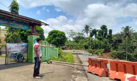 Seorang guru SDN 2 Parungponteng menunjukkan bagian tembok gerbang sekolah yang mengalami keretakan akibat bencana tanah longsor, Rabu (2/11/2022). Siswa di sekolah itu harus tetap belajar di ruang kelas yang terancam terkena tanah longsor susulan, lantaran jarak sekolah dengan lokasi tanah longsor hanya sekitar 3 meter.