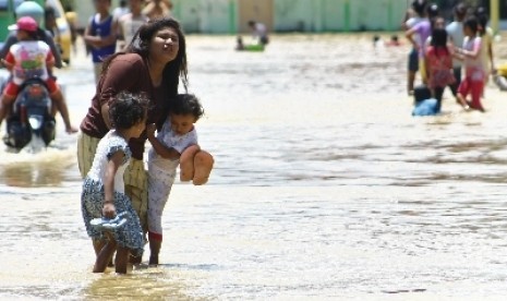 Seorang ibu bersama dua anaknya melewati genangan banjir di Sampang.