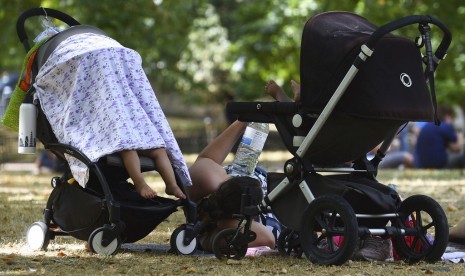 Seorang ibu dan anaknya berteduh di Taman St James di London pada Senin (23/7).