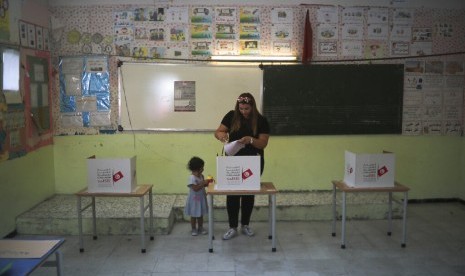 Seorang ibu dengan ditemani anaknya memberikan suara dalam pemilihan umum putaran pertama di Tunis, Tunisia, Ahad (15/9). 