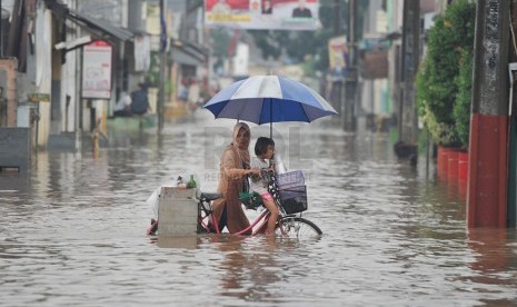  Seorang ibu membawa anaknya mendorong sepeda mereka melintasi banjir yang merendam perumahan Jatikramat Indah di Bekasi, Jawa Barat, Jumat (28/3).  (Republika/Edwin Dwi Putranto)