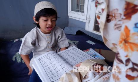 Seorang ibu mengajar anaknya mengaji. Anak perlu diperkenalkan etika.