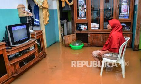 Seorang ibu menonton acara televisi di dalam rumahnya yang terendam banjir di Desa Tanjungsari, Kecamatan Sukaresik, Kabupaten Tasikmalaya, Jawa Barat, Kamis (14/1/2021). Akibat intensitas hujan yang tinggi, luapan air Sungai Citanduy dan Cikidang meluas hingga merendam 400 rumah warga di Dusun Bojongsoban dan Hegarsari dengan ketinggian mencapai sekitar 80 sentimeter hingga 1,5 meter.