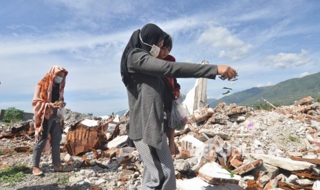 Seorang ibu sambil menggendong anak, menaburkan bunga di tempat hilangnya anggota keluarga mereka di lokasi bekas terdampak likuifaksi di Balaroa, Palu, Sulawesi Tengah.