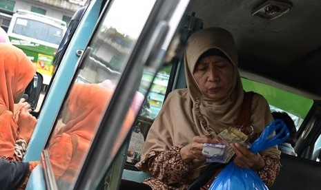 Seorang ibu sedang menghitung uang untuk membayar ongkos angkutan umum. 