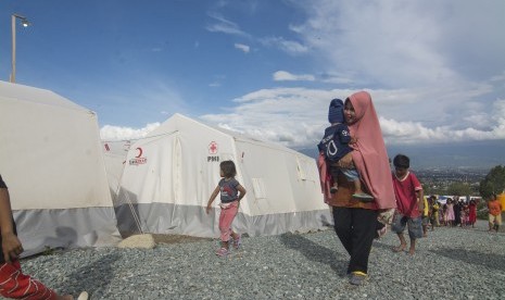 Seorang ibu terdampak bencana menggendong anaknya melintas di depan tenda sementara di kamp pengungsian Kelurahan Balaroa, Palu, Sulawesi Tengah, Sabtu (1/12/2018).