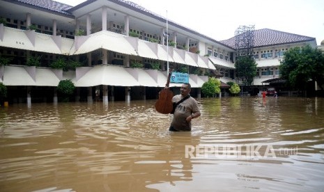  Seorang karyawan melintasi banjir yang menggenagi halaman sekolah SMA Negeri 8 , Bukit Duri, Jakarta (foto ilustrasi).