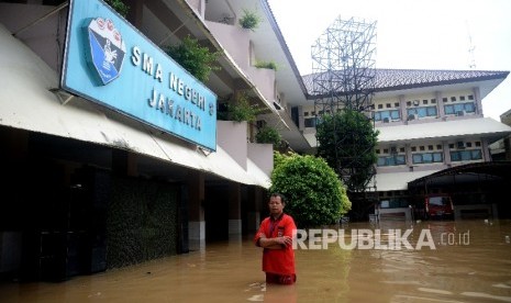  Seorang karyawan melintasi banjir yang menggenagi halaman sekolah SMA Negeri 8 , Bukit Duri, Jakarta, Kamis (16/2). 