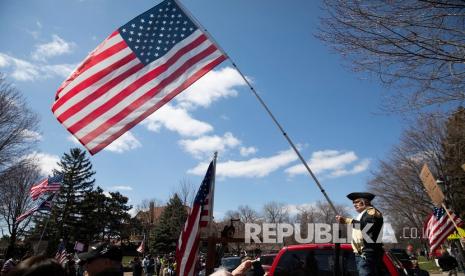 Seorang lelaki mengenakan pakaian gaya kolonial mengibarkan bendera saat demonstrasi Liberate Minnesota di St. Paul, Minn., Jumat (17/4). Semakin banyak protes yang dipentaskan di seluruh Amerika Serikat untuk menentang peraturan yang menganjurkan dirumah saja saat masa pandemic virus Corona. 