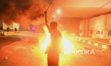 Seorang mahasiswa berdiri dekat api saat bentrok dengan petugas kepolisian saat berunjuk rasa di depan gedung DPR RI, Jakarta, Selasa (24/09/2019). 