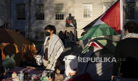 Seorang mahasiswa pengunjuk rasa berdiri di depan patung John Harvard, donatur utama pertama Harvard College, yang dibungkus bendera Palestina, di perkemahan mahasiswa yang memprotes perang di Gaza, di Universitas Harvard di Cambridge, Mass., 25 April 2024.