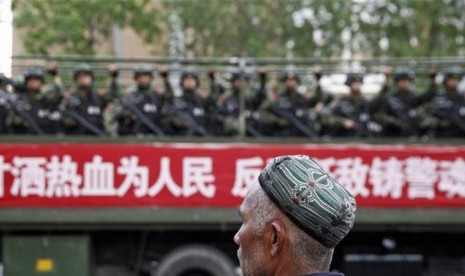 Seorang Muslim Uighur berada di depan militer yang patroli di wilayah Xinjiang.