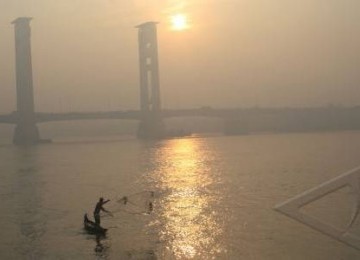 Seorang nelayan menjala ikan di Sungai Musi saat kabut asap menyelimuti Kota Palembang, Selasa (6/9).