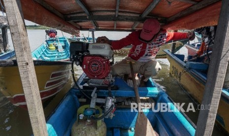 Seorang nelayan menyalakan mesin perahu yang telah dikonversi menggunakan bahan bakar elpiji.