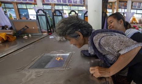 Seorang nenek mencoba melihat cucunya yang menjadi korban serangan pembunuhan massal melalui jendela peti mati di kuil Wat Rat Samakee di Uthai Sawan, timur laut Thailand, Minggu, 9 Oktober 2022. Seorang mantan polisi menerobos masuk. sebuah pusat penitipan anak di timur laut Thailand pada hari Kamis, menewaskan puluhan anak-anak prasekolah dan guru sebelum menembak lebih banyak orang saat ia melarikan diri.