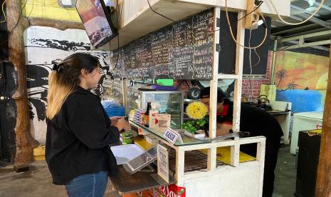 Seorang pedagang di kedai makanan dan minuman sedang melayani pembayaran dengan QRIS.