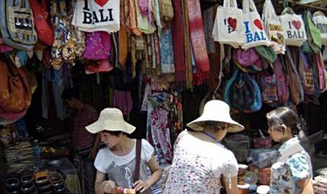 Seorang pedagang melayani wisatawan asing saat mereka berbelanja di Pasar Seni Ubud, Bali.