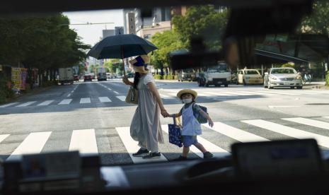 Seorang pejalan kaki menyeberang jalan dengan seorang anak terlihat melalui jendela taksi di Tokyo.