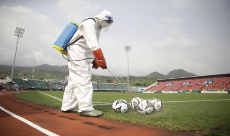 Seorang pejtugas yang mengenakan alat pelindung diri dari Covid-19 menyemprot bola dengan disinfektan sebelum pertandingan sepak bola di Piala Afrika 2021 di Stadium di Limbe, Kamerun, Rabu, 12 Januari 2022. Konfederasi Sepak Bola Afrika (CAF), Rabu (26/1/2022) menyatakan, kondisi lapangan yang buruk menyebabkan tempat pertandingan perempat final dan semifinal Piala Afrika 2021 dipindahkan.  