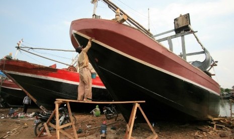 Seorang pekerja sedang memperbaiki kapal yang rusak. Bantuan pemerintah berupa kapal fiber banyak dikeluhkan nelayan karena bingung mengoperasikan