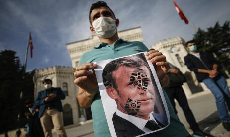  Seorang pemuda memegang foto Presiden Prancis Emmanuel Macron, dicap dengan tanda sepatu, selama protes terhadap Prancis di Istanbul, Ahad, 25 Oktober 2020.