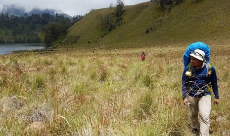 Seorang pendaki berjalan di hamparan luas dengan latar Ranu Kumbolo