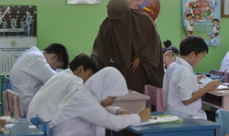 Seorang pengawas membantu peserta mengisi identitas peserta sebelum mengikuti ujian paket A atau setara SD di SDN Gondangdia 1 Pagi, Jakarta, Senin (18/5).