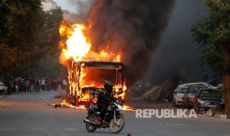 Seorang pengendara melintasi bus yang terbakar saat maasa berunjukrasa penentang Revisi UU Kewarganegaraan India di New Delhi, India, Ahad (15/12)