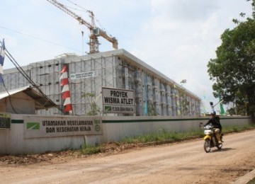 Seorang pengendara sepeda motor melintas di depan wisma atlet yang saat ini dalam proses pembangunan tahap akhir, di Jakabaring, Palembang.