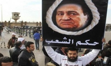 Seorang pengunjuk rasa, keluarga korban yang tewas dalam Revolusi Mesir, membentangkan poster bergambar mantan Presiden Hosni Mubarak dengan latar belakang tali gantungan bertuliskan hukum rakyat, Senin (2/1).