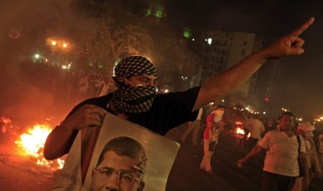 Seorang pengunjuk rasa memegang poster Presiden Mursi saat berunjuk rasa menolak kudeta militer di pusat kota Kairo, Senin (15/7).     (AP/Khalil Hamra)