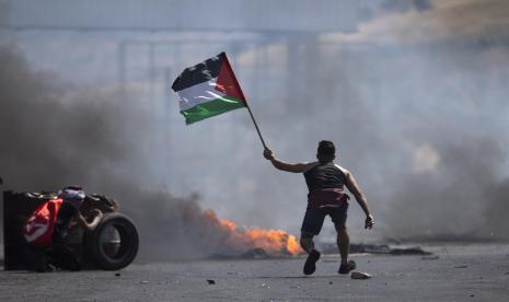 Seorang pengunjuk rasa mengibarkan bendera Palestina selama bentrokan dengan pasukan Israel di pos pemeriksaan Hawara, selatan kota Nablus, Tepi Barat, Jumat, 14 Mei 2021. 