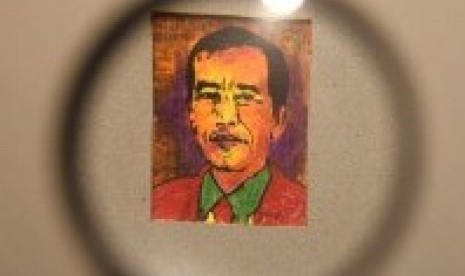 Seorang pengunjung menggunakan kaca pembesar untuk mengamati lukisan mini berukuran 3x4 cm bergambar Presiden Joko Widodo karya Jupri Abdullah saat pembukaan pameran di Surabaya, Jawa Timur, Jumat (2/11).