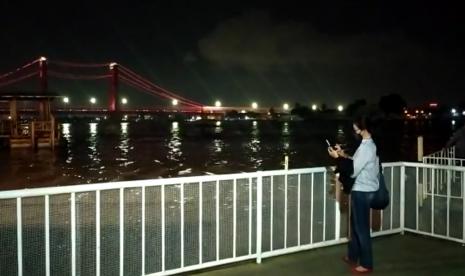 Seorang pengunjung menikmati pemandangan Jembatan Ampera yang membentang di Sungai Musi dari Riverside Restaurant.