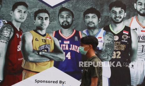 Seorang penonton yang mengenakan masker melintas di depan baliho Indonesia Basketball League (IBL) 2020 Seri VII di GOR Bimasakti, Malang, Jawa Timur, Jumat (13/3/2020).