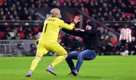 Seorang penyusup lapangan menyerang kiper Sevilla Marko Dmitrovic (kiri) dalam pertandingan playoff Liga Europa di markas PSV Eindhoven. Pria tersebut dijatuhi hukuman kurungan dan larangan memasuki Stadion Phillips, markas PSV, selama 40 tahun.