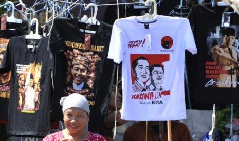 Seorang perempuan berdiri di depan kios kaki lima yang menjual kaos bergambar Jokowi-JK adalah Kita di Surabaya, Jawa Timur, Ahad (29/6). 