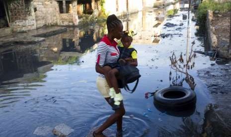 Seorang perempuan berjalan di jalanan yang penuh kotoran saat ia menggendong putrinya ke sekolah di daerah kumuh Cite Soleil di Port-au-Prince, Haiti. Foto diambil pada Rabu (3/10).