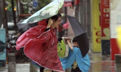 Seorang perempuan dan anaknya memegang payung mereka dengan erat, saat angin kencang yang dipicu oleh topan Usagi bergerak mendekati Taipei, Taiwan, Sabtu  (21/9).