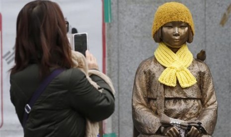 Seorang perempuan mengambil gambar patung seorang gadis yang melambangkan korban budak seks Jepang saat PD II di depan Kedubes Jepang di Seoul, Korsel, Selasa, 29 Desember 2015.