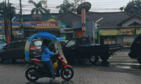 Seorang perempuan menggunakan mantel hujan untuk motor melintas di kawasan Sawangan, Depok. Pelebaran Jalan Raya Sawangan dilakukan untuk mengatasi kemacetan. Ilustrasi.