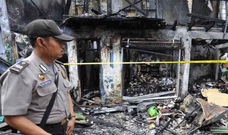 Seorang personel kepolisian melintasi bangunan yang terbakar akibat tawuran antarwarga di Johar Baru, Jakarta Pusat, Senin (18/11).