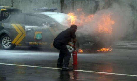 Seorang petugas berusaha memadamkan api yang membakar mobil polisi di Jalan Gunung Sahari, Jakarta Pusat, Jumat ( 18/1).