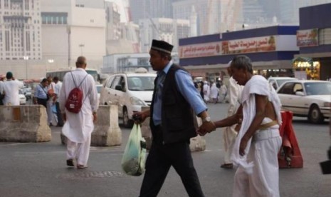 Seorang petugas haji Indonesia yang bertugas di Sektor Khusus Masjidil Haram sedang menuntun jamaah sepuh yang tersesat. 